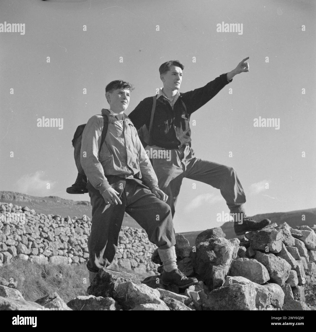 GIOVANI ESCURSIONISTI NELLO YORKSHIRE: IL LAVORO DELLA YOUTH HOSTEL ASSOCIATION IN WARTIME, MALHAM, YORKSHIRE, INGHILTERRA, REGNO UNITO, 1944 - due ragazzi si fermano al sole durante una passeggiata attraverso la campagna dello Yorkshire per ammirare il panorama, uno di loro indica qualcosa in lontananza. Hanno iniziato a camminare da un ostello della gioventù, probabilmente a Malham. , Foto Stock