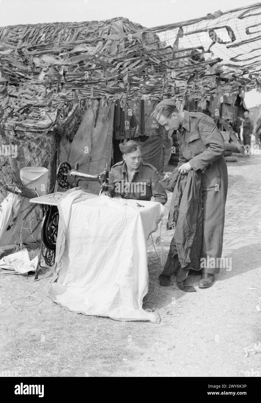 ROYAL AIR FORCE: 2ND TACTICAL AIR FORCE, 1943-1945. - A Un macchinista di cucito della No. 84 Group Support Unit, gli viene chiesto se può riparare le tute strappate di un caporale a Merston, Sussex. , Royal Air Force, Group, 84, Royal Air Force, unità di manutenzione, 201 Foto Stock