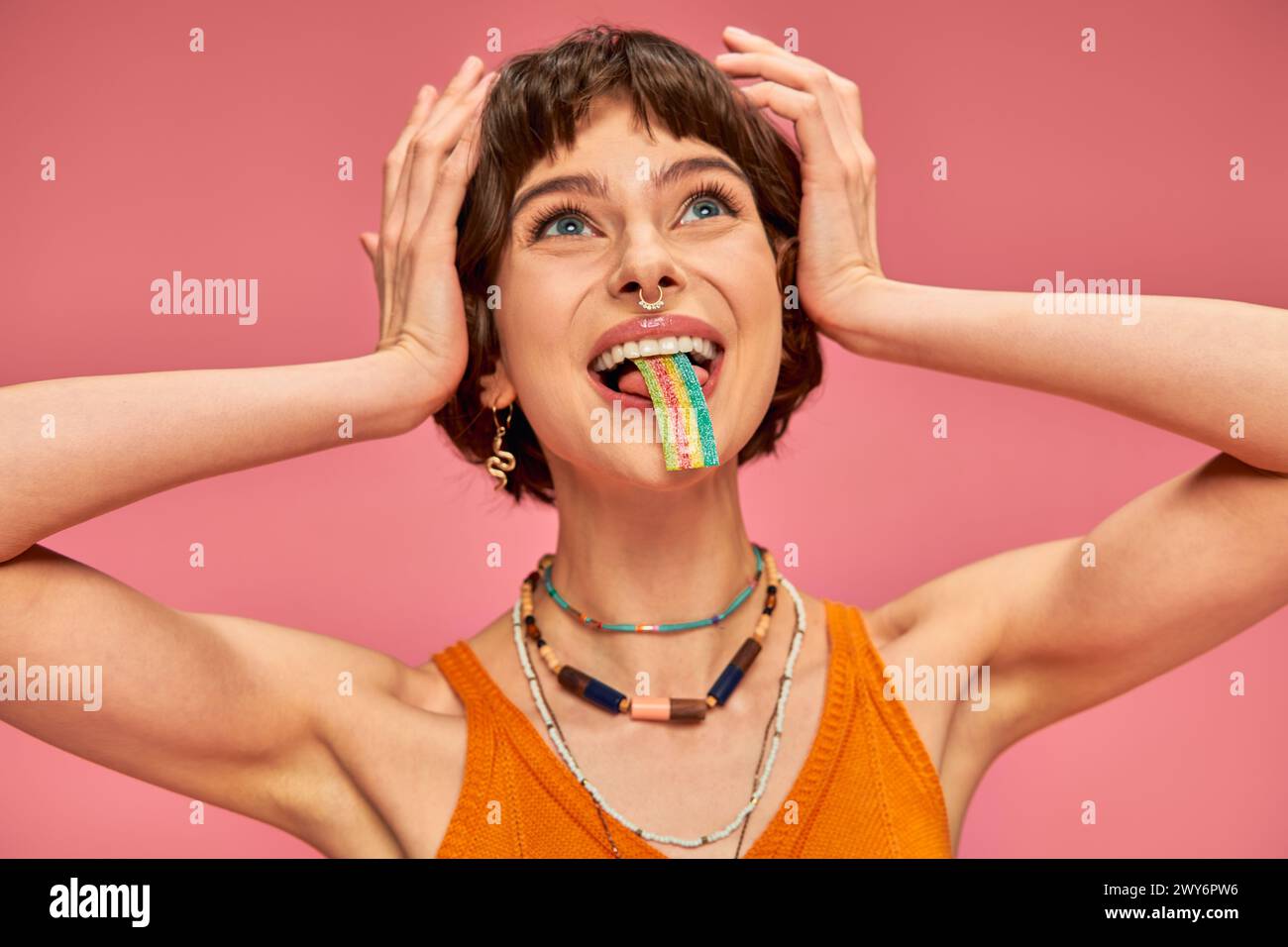 giovane donna felice che assaggia una striscia di caramelle dolci e acide sulla lingua, sfondo rosa Foto Stock