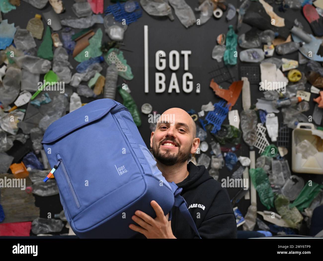 Mainz, Germania. 4 aprile 2024. Benjamin Mandos, fondatore della Got Bag, con sede a Mainz, si trova di fronte a una parete con uno zaino su cui sono stati incollati rifiuti di plastica intorno al logo del marchio. Fondata nel 2016, la Start-up utilizza per i suoi zaini e valigie tessuti realizzati con plastica riciclata proveniente dal mare o dalle aree di mangrovie, nota come plastica a impatto oceanico. Credito: Arne Dedert/dpa/Alamy Live News Foto Stock