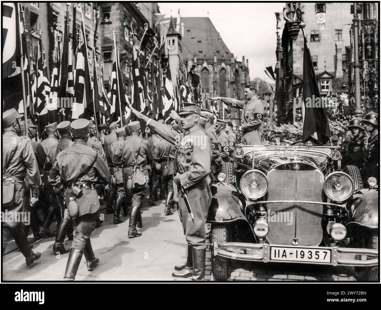 ADOLF HITLER Vintage Nurnberg Norimberga Rally 1935, Germania - SA Sturmabteilung milizia politica truppe del partito nazista, marciano oltre Adolf Hitler durante una parata NSDAP in città. Nel 1930 Adolf Hitler indossa una fascia di svastica in parata militare, in piedi in auto Mercedes libera dà il saluto a Heil Hitler per passare le truppe Sturmabteilung in marcia, con le sue guardie Waffen SS in piedi dietro Norimberga Norimberga Germania Foto Stock