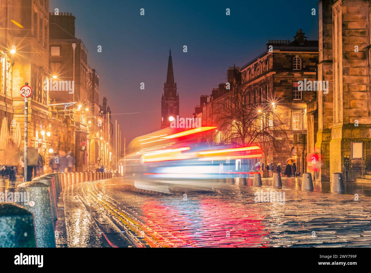 Le luci dell'auto percorrono la strada acciottolata High Street di notte lungo un tratto conosciuto come Royal Mile nella città vecchia di Edimburgo, Scozia Foto Stock