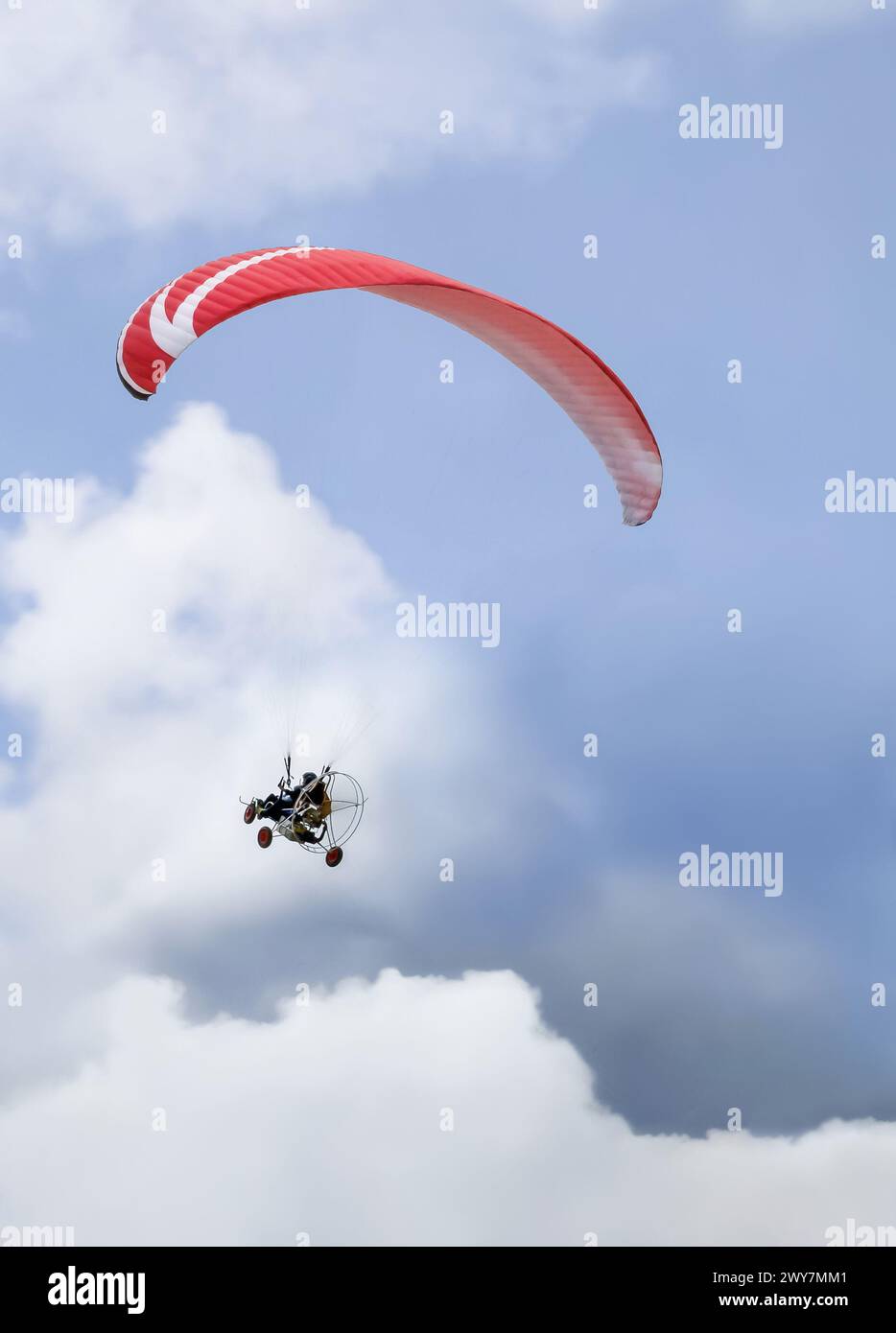 Persona su un paramotore con parapendio rosso che vola tra le nuvole del cielo blu. Foto Stock