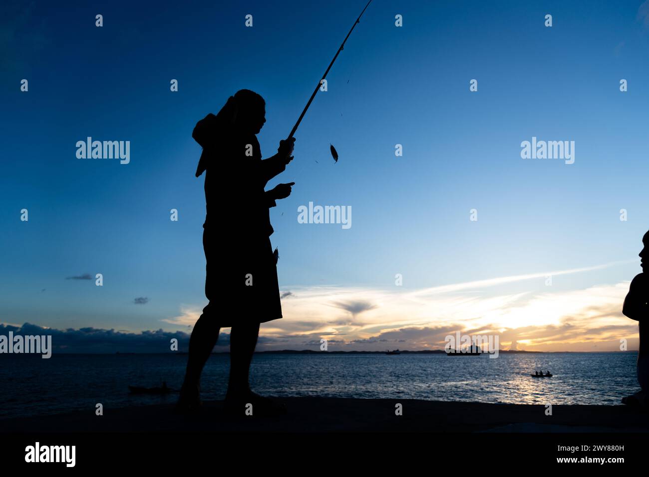 Salvador, Bahia, Brasile - 13 aprile 2019: Il pescatore viene visto in silhouette al tramonto a Ponta do Humaita nella città di Salvador, Bahia. Foto Stock