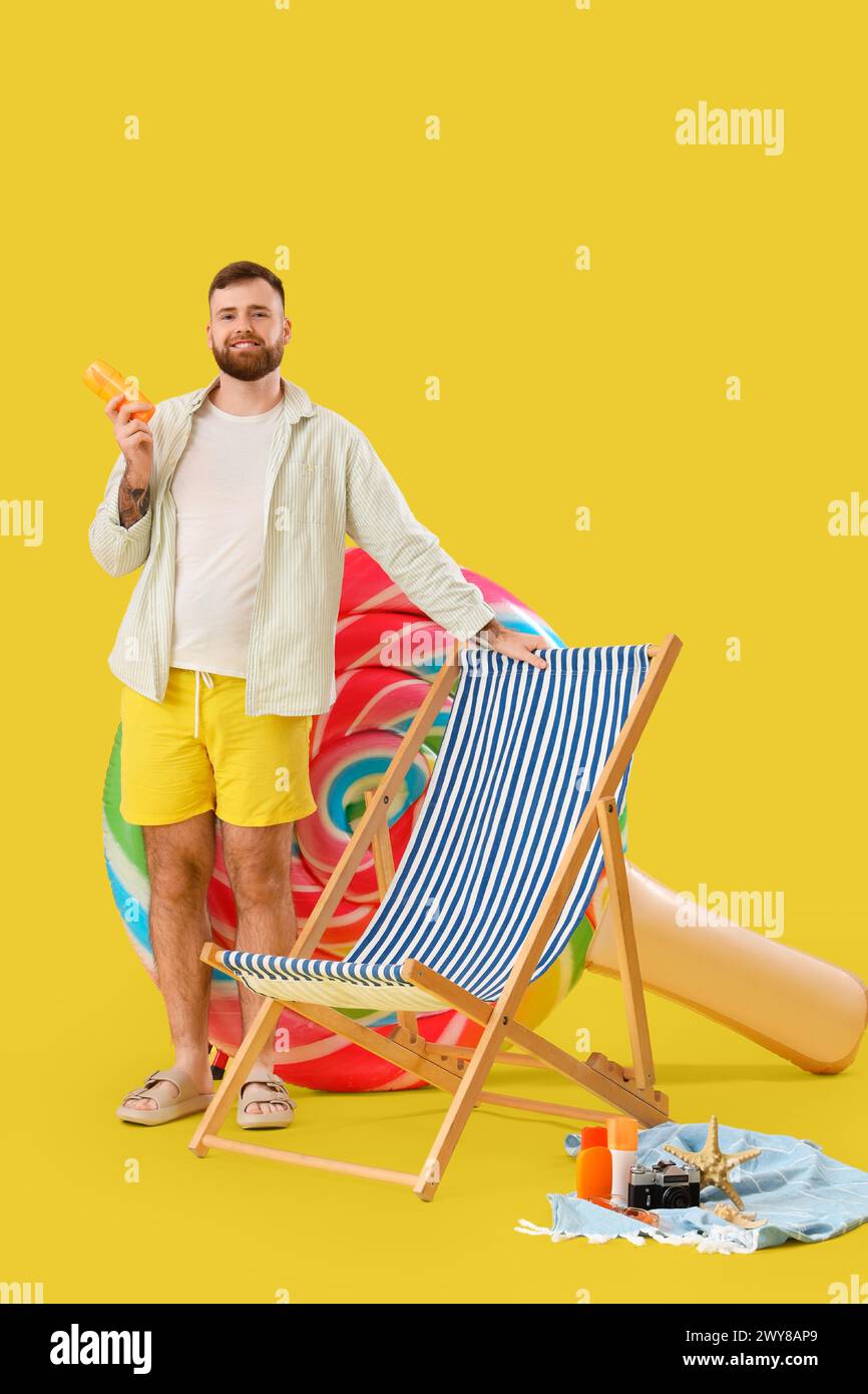 Giovane uomo con materasso gonfiabile a forma di lecca lecca e sdraio su sfondo giallo Foto Stock