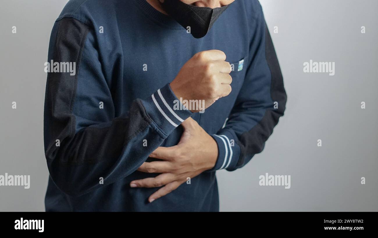 qualcuno che indossa una maschera per la bocca che tossisce e gli tiene il petto perché è malato Foto Stock