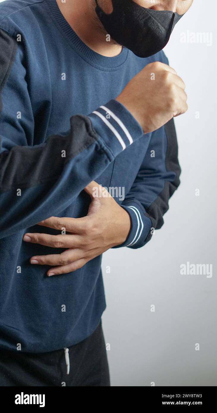 qualcuno che indossa una maschera per la bocca che tossisce e gli tiene il petto perché è malato Foto Stock