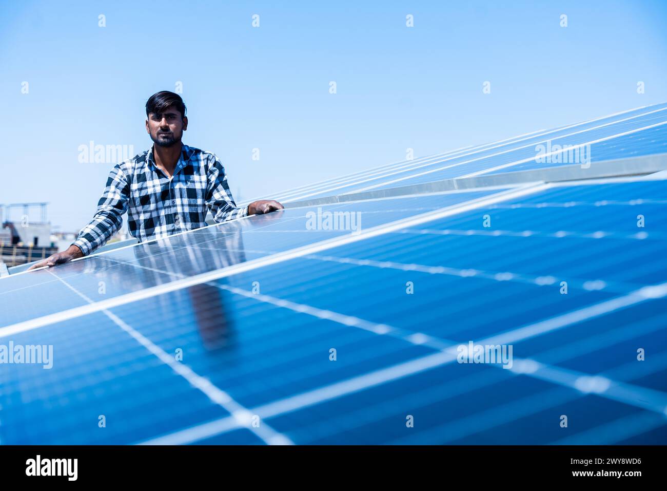 Lavoratore indiano che installa pannelli solari sul tetto della casa. Manutenzione del sistema di pannelli fotovoltaici. Concetto di energia alternativa, rinnovabile.Copia spazio Foto Stock