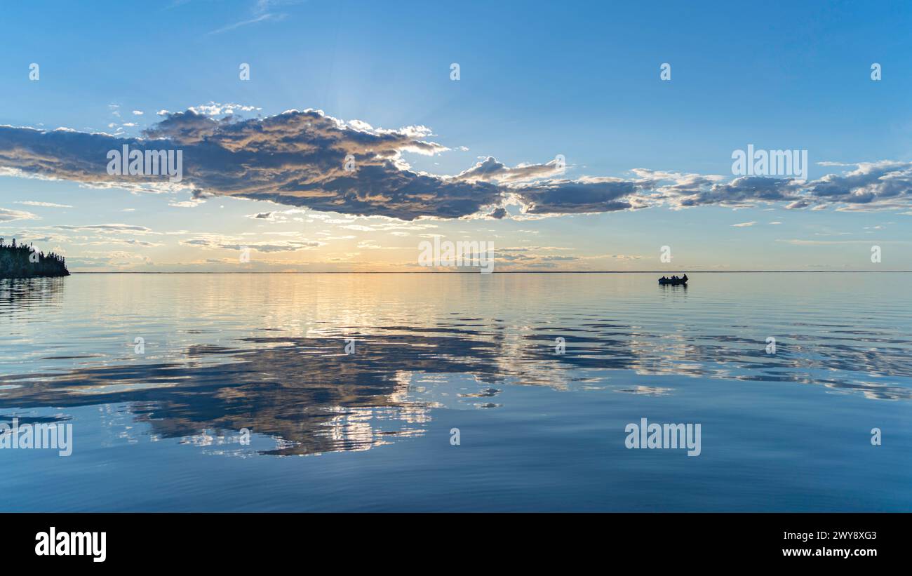 tramonto panoramico con nuvole su un grande lago calmo con una barca in lontananza Foto Stock