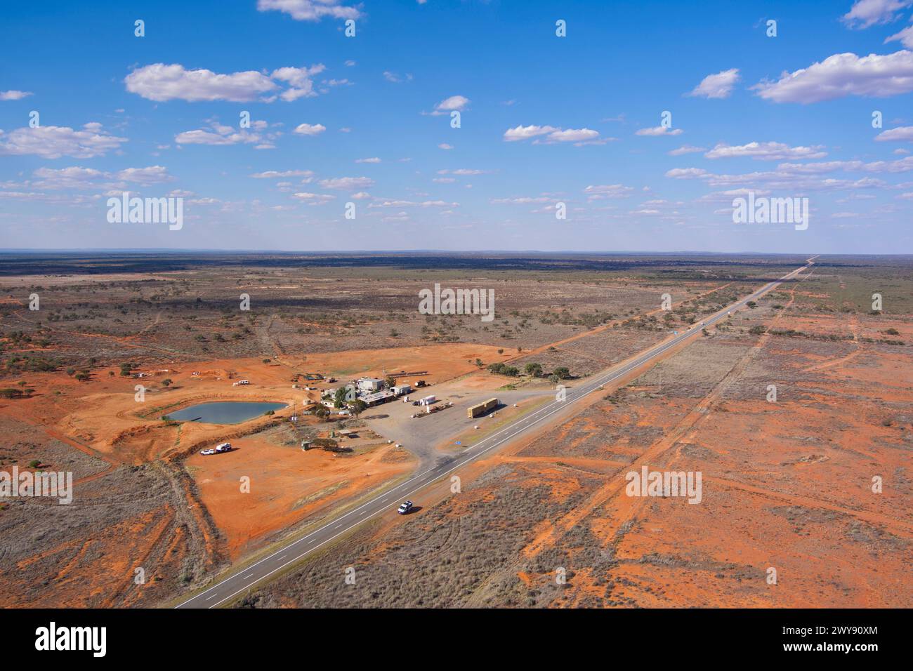 Vista aerea di un'autostrada che attraversa un paesaggio arido con un piccolo insediamento lungo la strada e un cielo azzurro Foto Stock