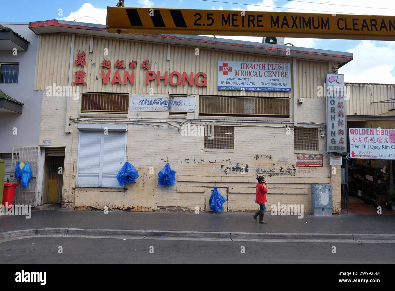 Van Phong, un retro del muro dell'edificio con borse di plastica blu appese ai ganci, una donna con una camicia rossa parla con un telefono cellulare. Foto Stock