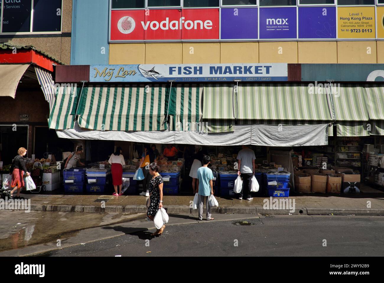 Clienti di un mercato del pesce con facciata in strada aperta e tende da sole in tela a righe a Dutton Lane, Cabramatta, Western Sydney Foto Stock