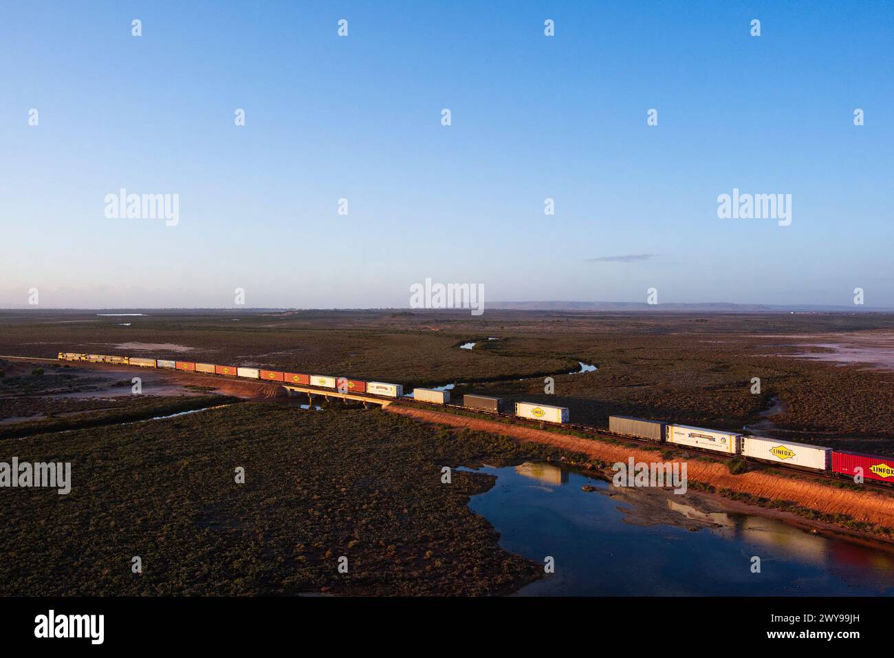 Vista aerea di un treno merci intermodale che attraversa un vasto paesaggio desertico al crepuscolo vicino a Port Augusta, Australia meridionale Foto Stock