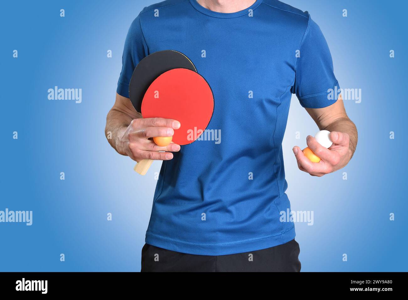 Dettaglio del giocatore di ping pong con abbigliamento sportivo e racchette e palle da gioco con le mani su sfondo blu isolato. Foto Stock