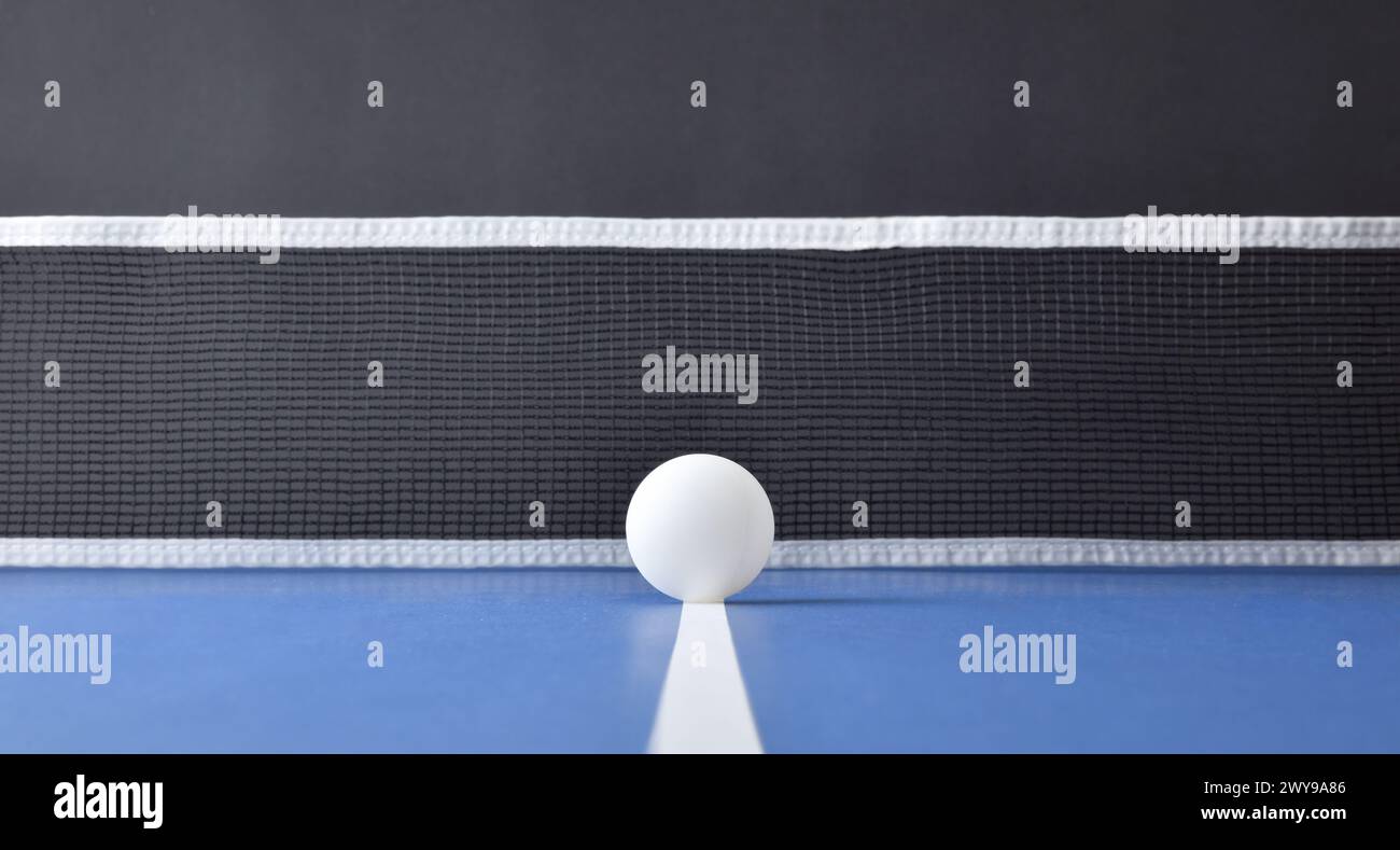 Concetto di gioco da ping pong con palla bianca centrata sulla linea centrale di un tavolo da gioco blu con la rete dietro e sfondo nero isolato. Vista frontale. Foto Stock