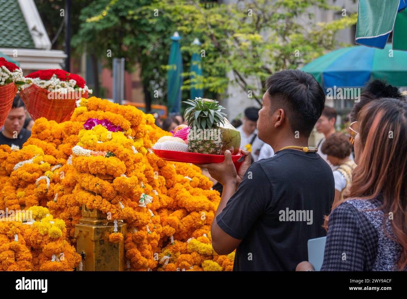 Nel cuore del centro di Bangkok, presso il Santuario Erawan, un uomo asiatico offre le sue preghiere consegnando un cestino pieno di frutta acquistata come offerta. Bangkok, Thailandia. Foto Stock