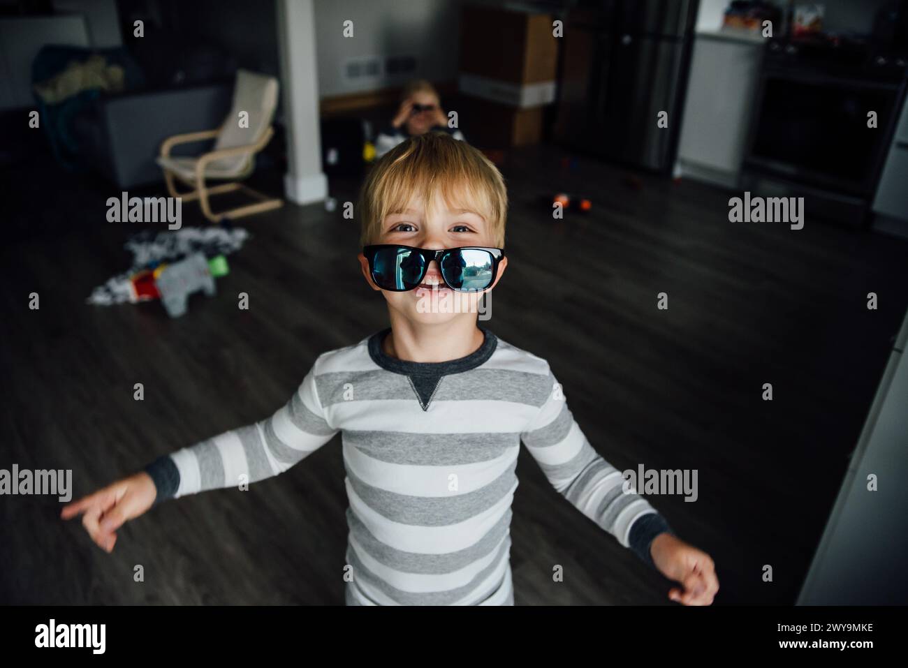 Ritratto di un ragazzo sorridente che guarda fuori da dietro gli occhiali da sole in casa Foto Stock