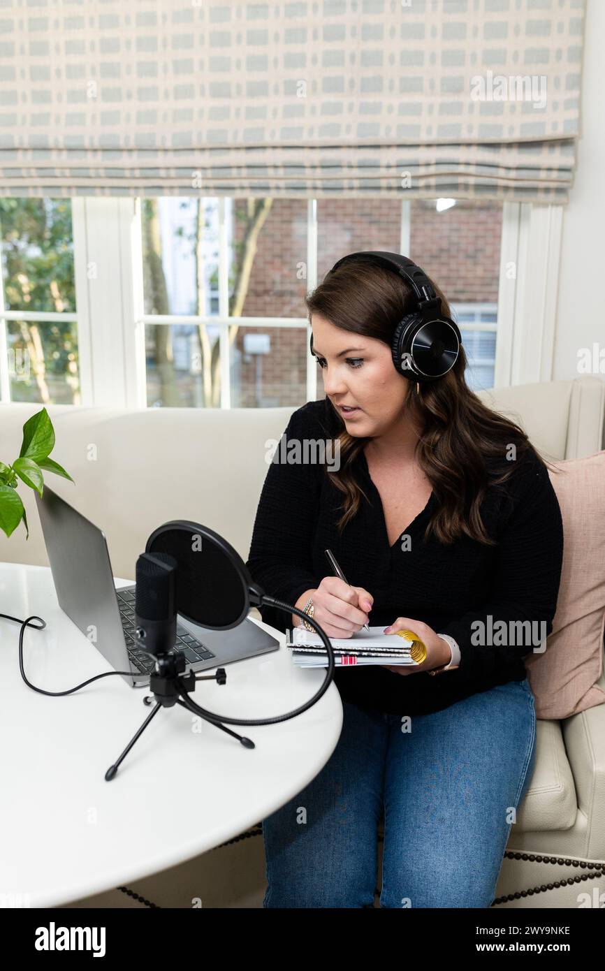 Podcasting e appunti di una donna concentrata durante la registrazione a casa Foto Stock