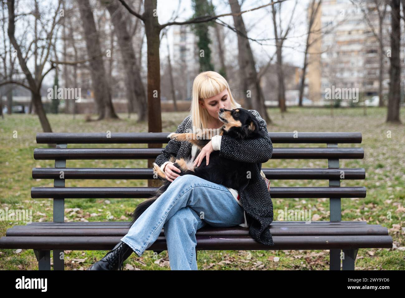 La giovane generazione Z hipster ragazza seduta in un parco su una panchina con il suo cane adottato, che ha salvato dalla strada dalla fame, e gli dà amore Foto Stock