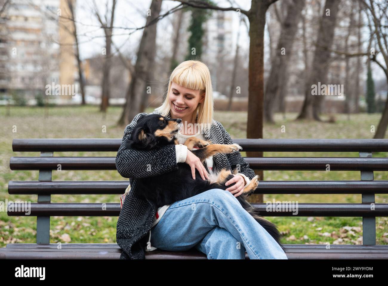 La giovane generazione Z hipster ragazza seduta in un parco su una panchina con il suo cane adottato, che ha salvato dalla strada dalla fame, e gli dà amore Foto Stock