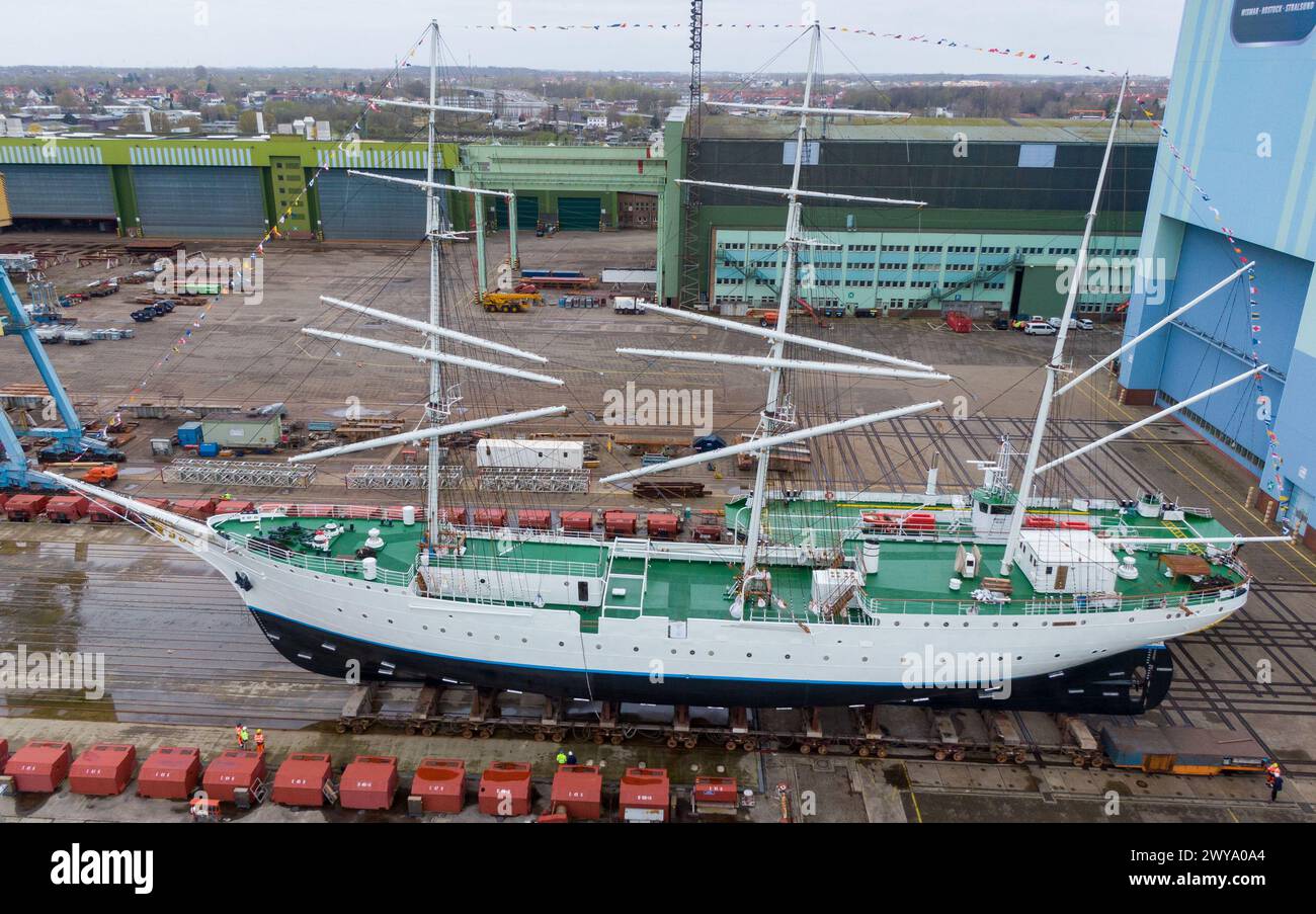 5 aprile 2024, Meclemburgo-Pomerania occidentale, Stralsund: Il "Gorch Fock 1" ha lasciato la sala di costruzione ed è in piedi sull'ascensore della nave (vista aerea con drone). Dopo aver trascorso diversi mesi nella grande sala di costruzione navale del cantiere Volkswerft di Stralsund, il tradizionale veliero "Gorch Fock 1", vecchio di 90 anni, è tornato all'aria aperta. Lo stesso giorno, l'ex nave addestratrice a vela ha lasciato la sala del cantiere con un nuovo, scintillante rivestimento bianco di vernice, dove i costruttori navali hanno effettuato estesi lavori di ristrutturazione. In futuro, la nave sarà nuovamente aperta al pubblico come Foto Stock