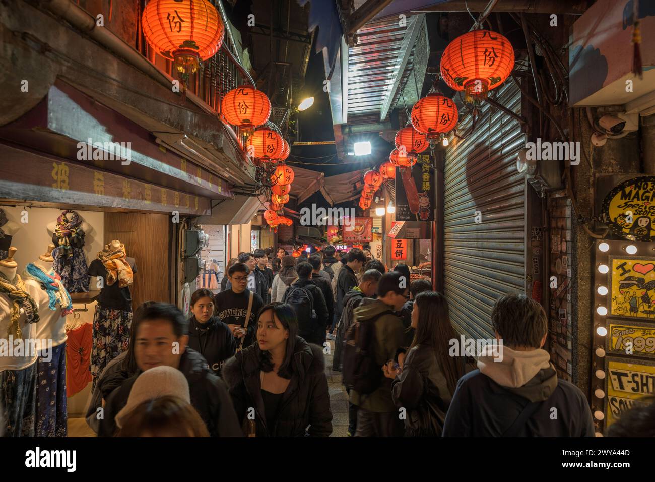 Un affollato mercato notturno di Jiufen illuminato da lanterne rosse con negozi e persone Foto Stock