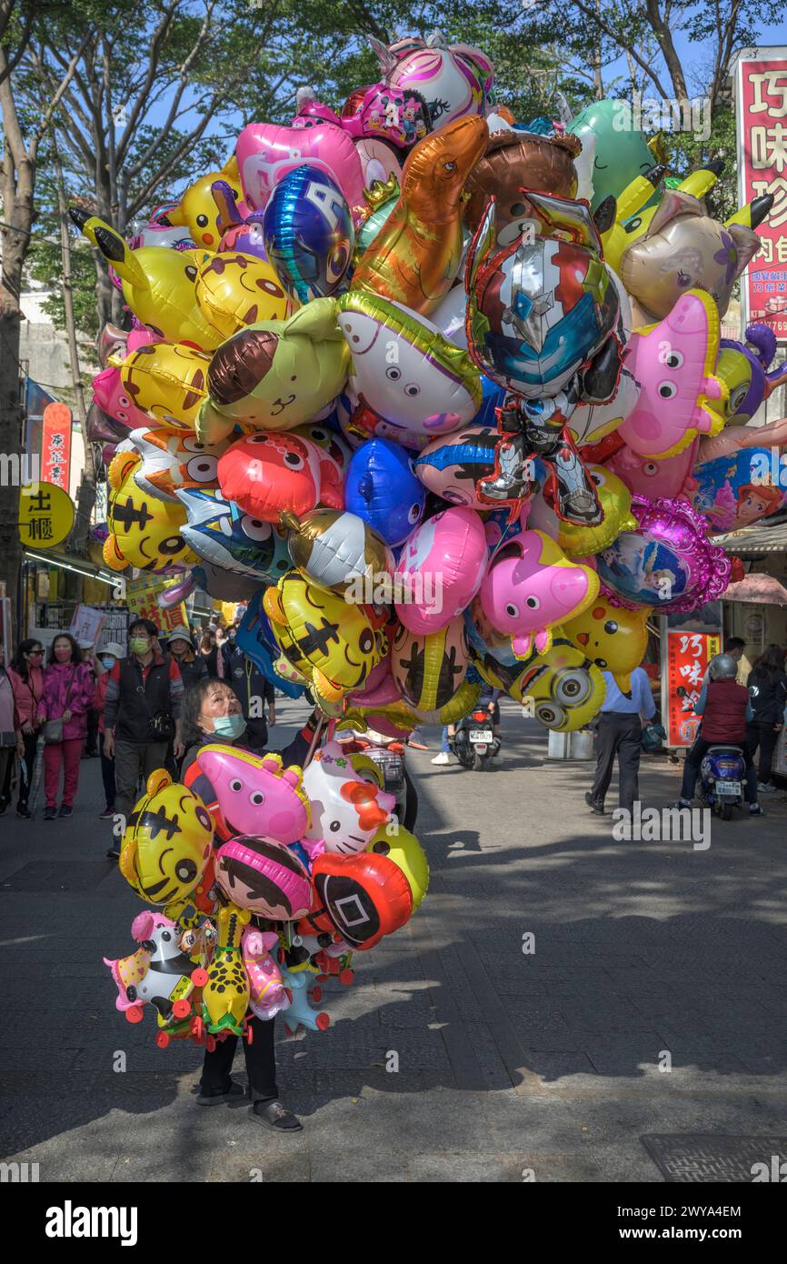 Una gamma festosa di vari palloncini colorati tenuti da un venditore in una vivace scena di strada a Lukang Foto Stock