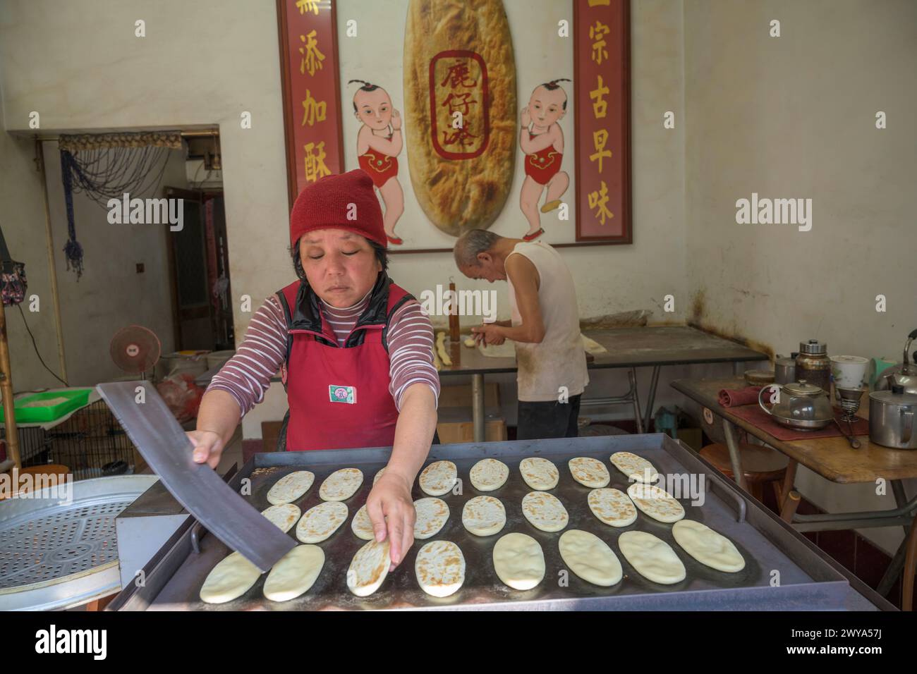 Una coppia di anziani che prepara il pane in un piccolo negozio con un cartello cinese Foto Stock