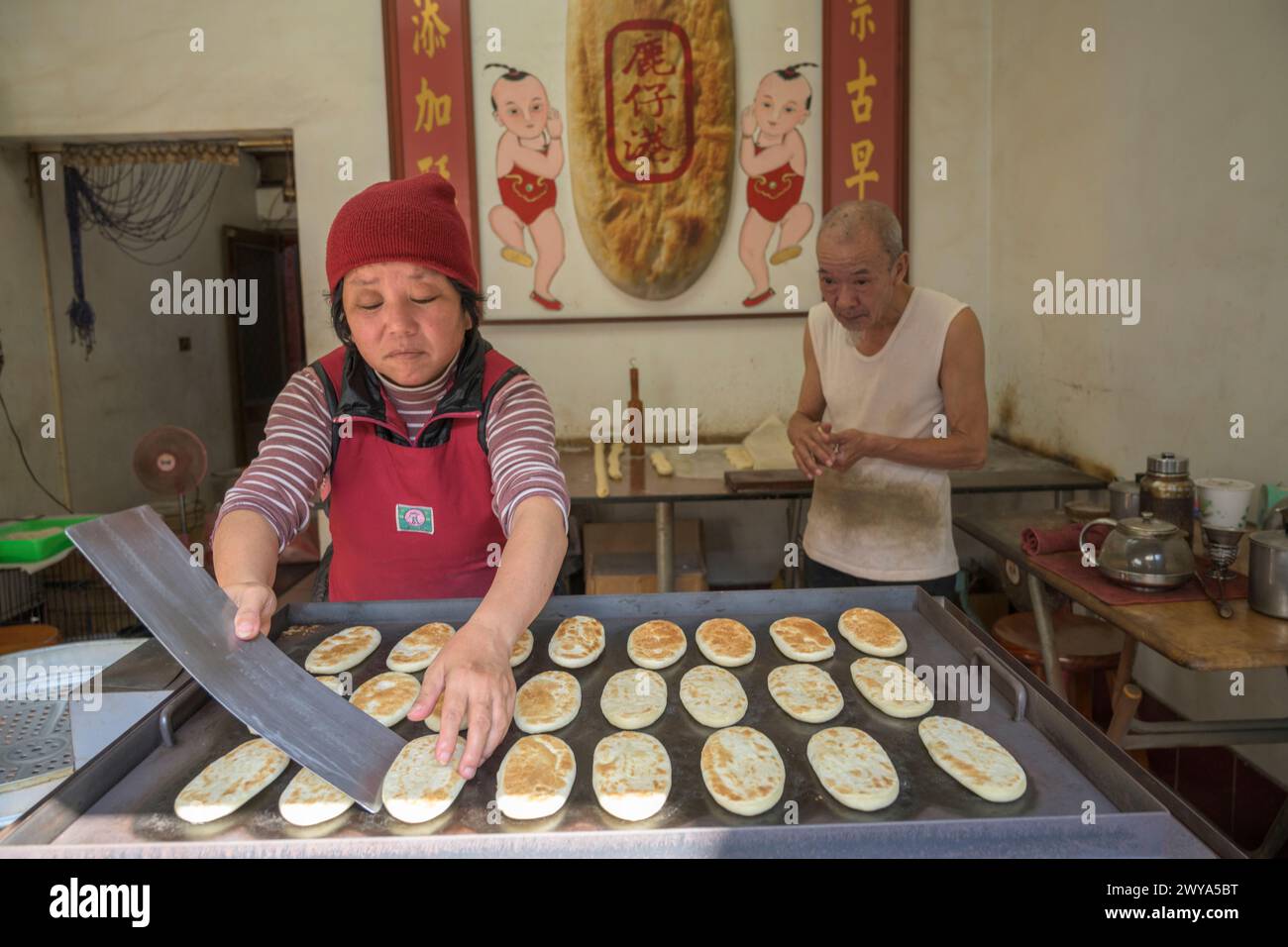 Una coppia di anziani che prepara il pane in un piccolo negozio con un cartello cinese Foto Stock