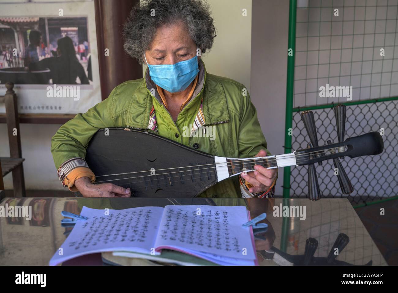 Donna anziana che suona un tradizionale strumento a corde cinese con una maschera Foto Stock