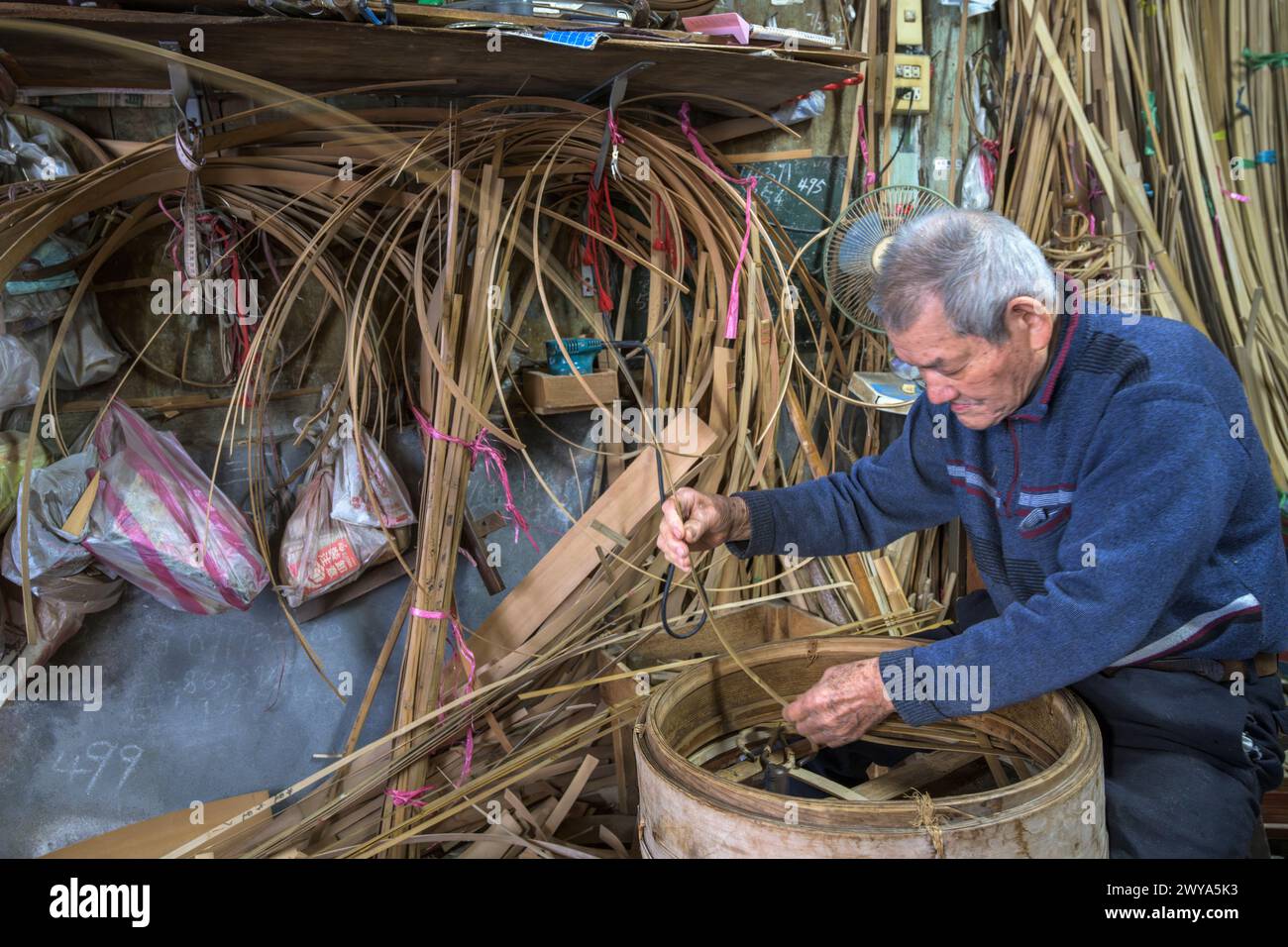 Un anziano artigiano intreccia meticolosamente strisce di bambù per creare un cestino tradizionale nella sua bottega nella città di Lukang Foto Stock