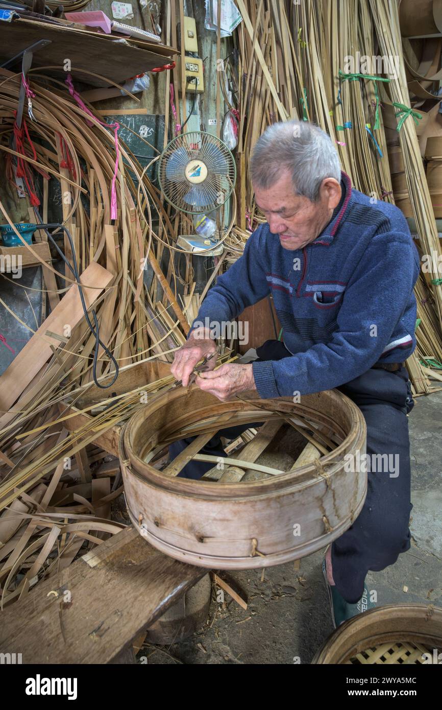 Un anziano artigiano intreccia meticolosamente strisce di bambù per creare un cestino tradizionale nella sua bottega nella città di Lukang Foto Stock