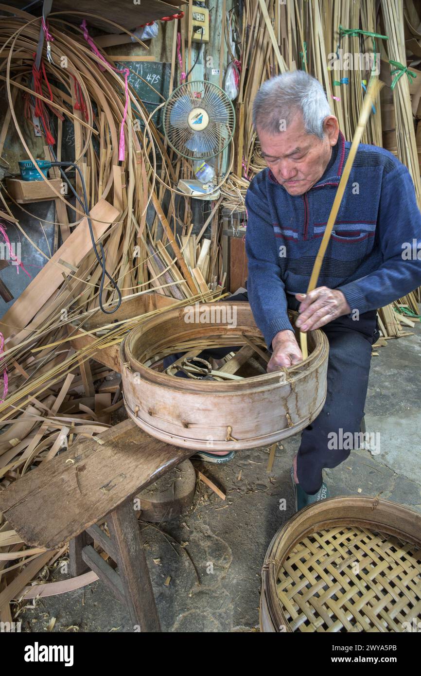 Un anziano artigiano intreccia meticolosamente strisce di bambù per creare un cestino tradizionale nella sua bottega nella città di Lukang Foto Stock