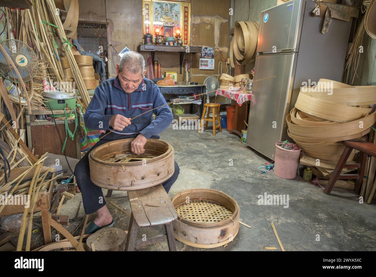 Un anziano artigiano intreccia meticolosamente strisce di bambù per creare un cestino tradizionale nella sua bottega nella città di Lukang Foto Stock
