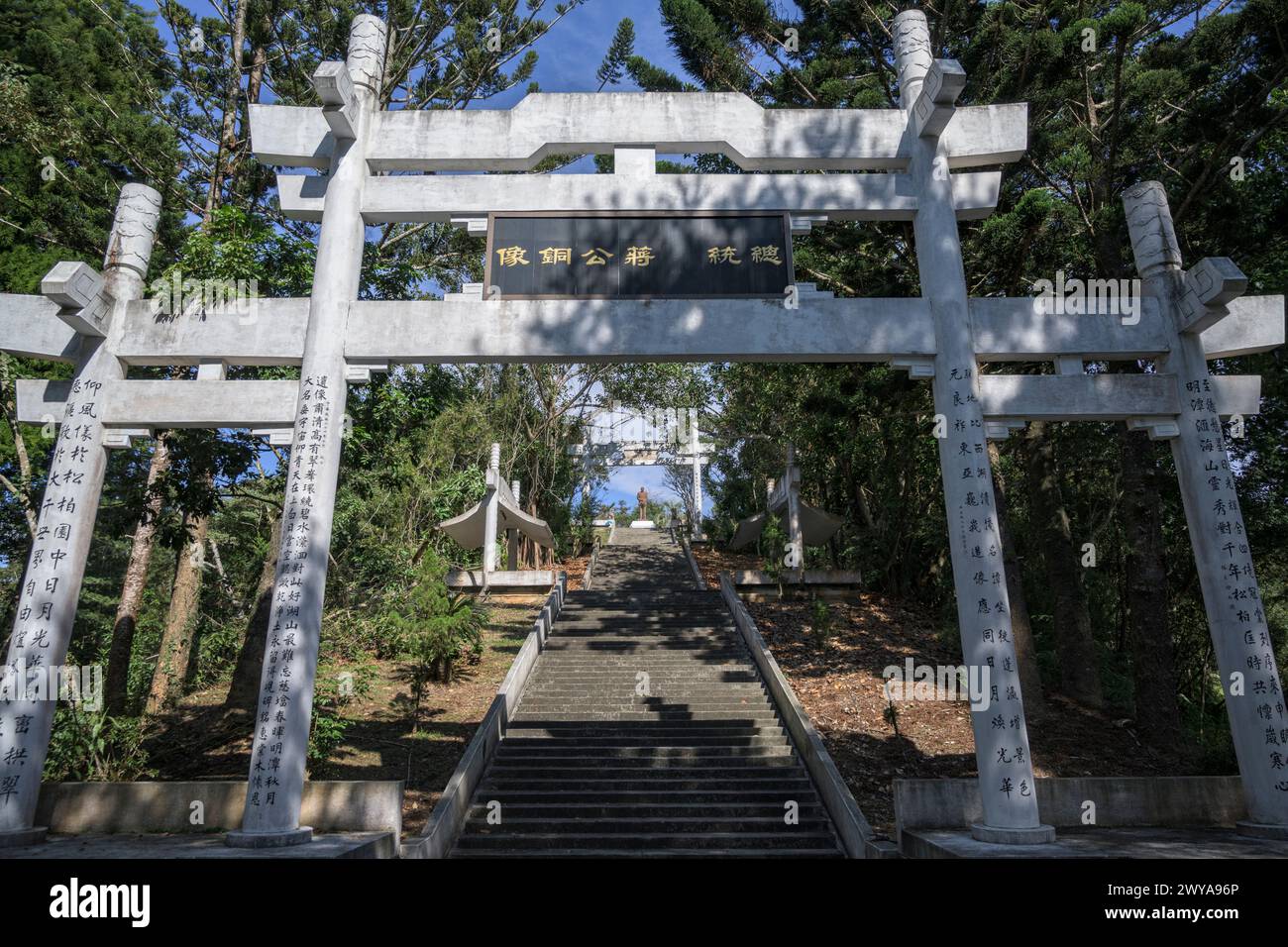 Una porta orientale Torii con testo Kanji, che conduce ad un'area sacra circondata da lussureggiante vegetazione e cieli azzurri chiari vicino al lago Sun Moon Foto Stock