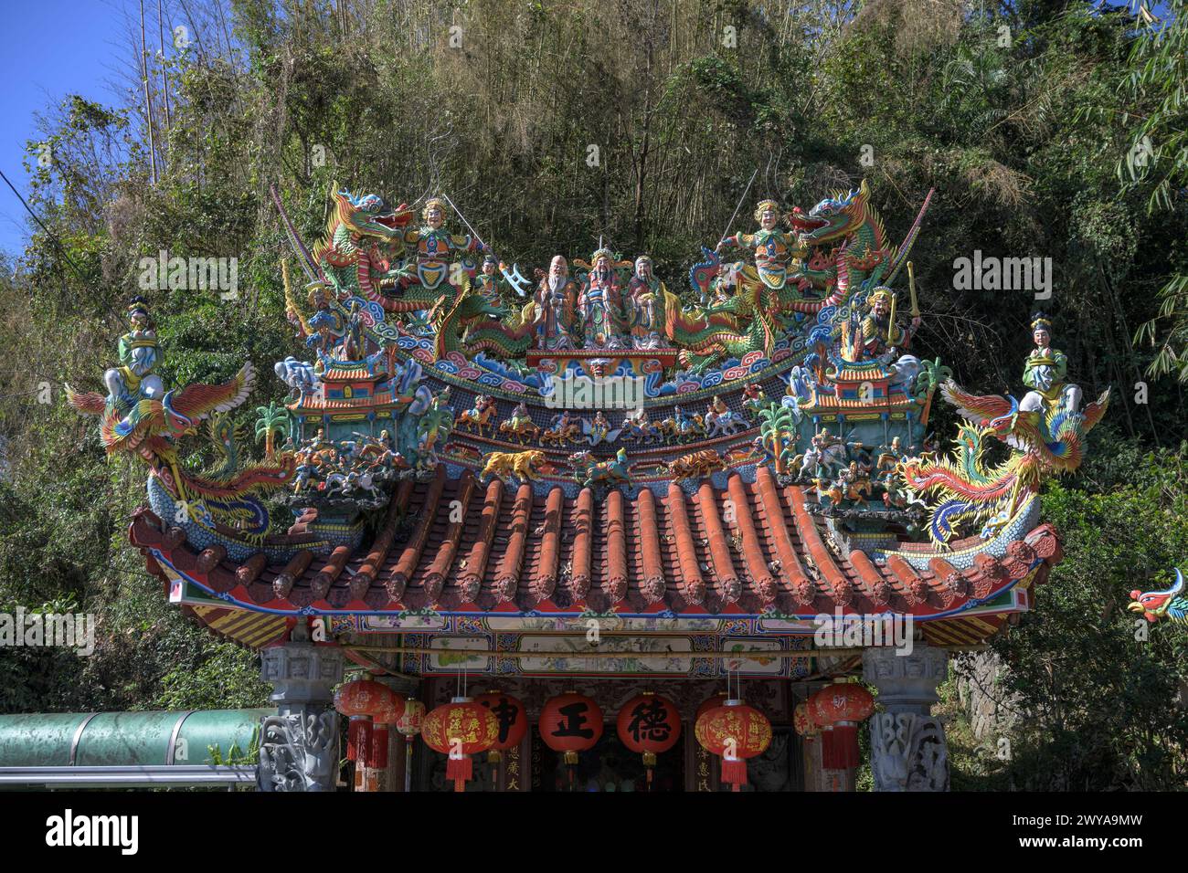 Una vibrante scultura di drago che adorna il tetto di un tempio con un cielo blu e uno sfondo di pini Foto Stock