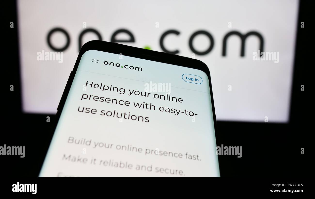 Smartphone con sito web della società di web hosting One.com Group davanti al logo aziendale. Mettere a fuoco in alto a sinistra sul display del telefono. Foto Stock