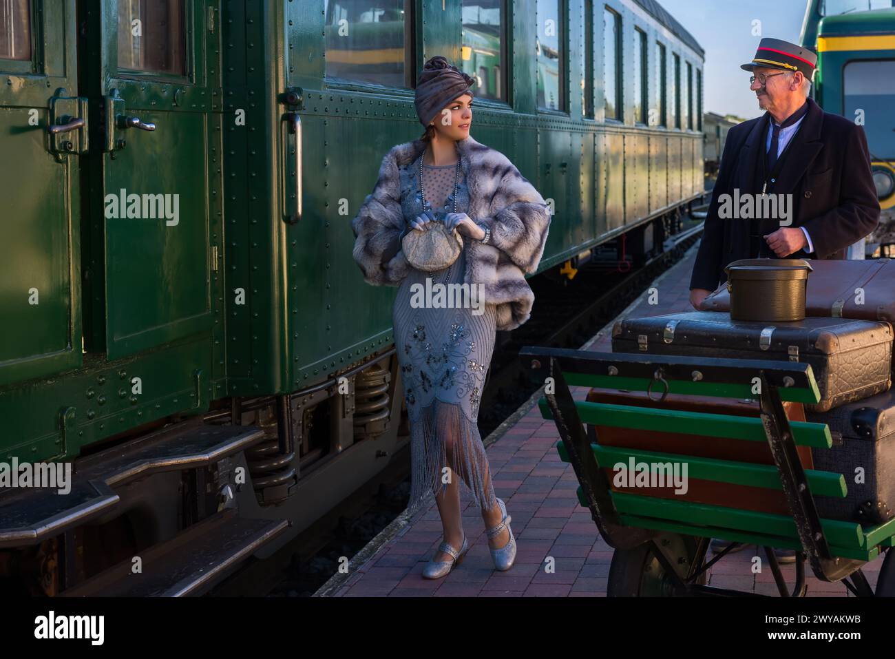 Scena di rievocazione sulla piattaforma vicino a un autentico vagone ferroviario di prima classe 1927 dove una donna di lusso 1920s sta aspettando il suo bagaglio Foto Stock