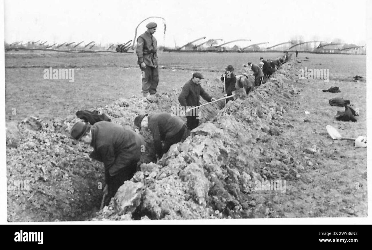 I tedeschi scavano una trincea per cavi telefonici sotto la supervisione del britannico NCO Cpl MacDougall di Percy Main, North Shields, documentato dal 21st Army Group dell'esercito britannico. Foto Stock