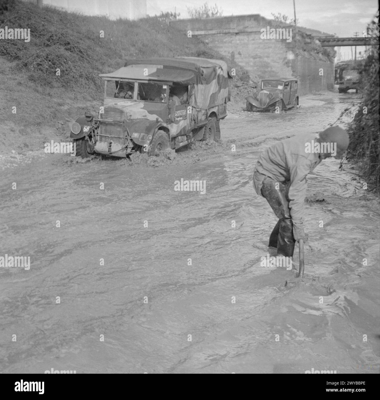 Un ingegnere americano canalizza l'acqua da una strada allagata mentre un camion britannico Fordson WOT2 15-cwt attraversa durante le operazioni in Italia il 17 novembre 1943, illustrando le sfide logistiche del trasporto in tempo di guerra. Foto Stock
