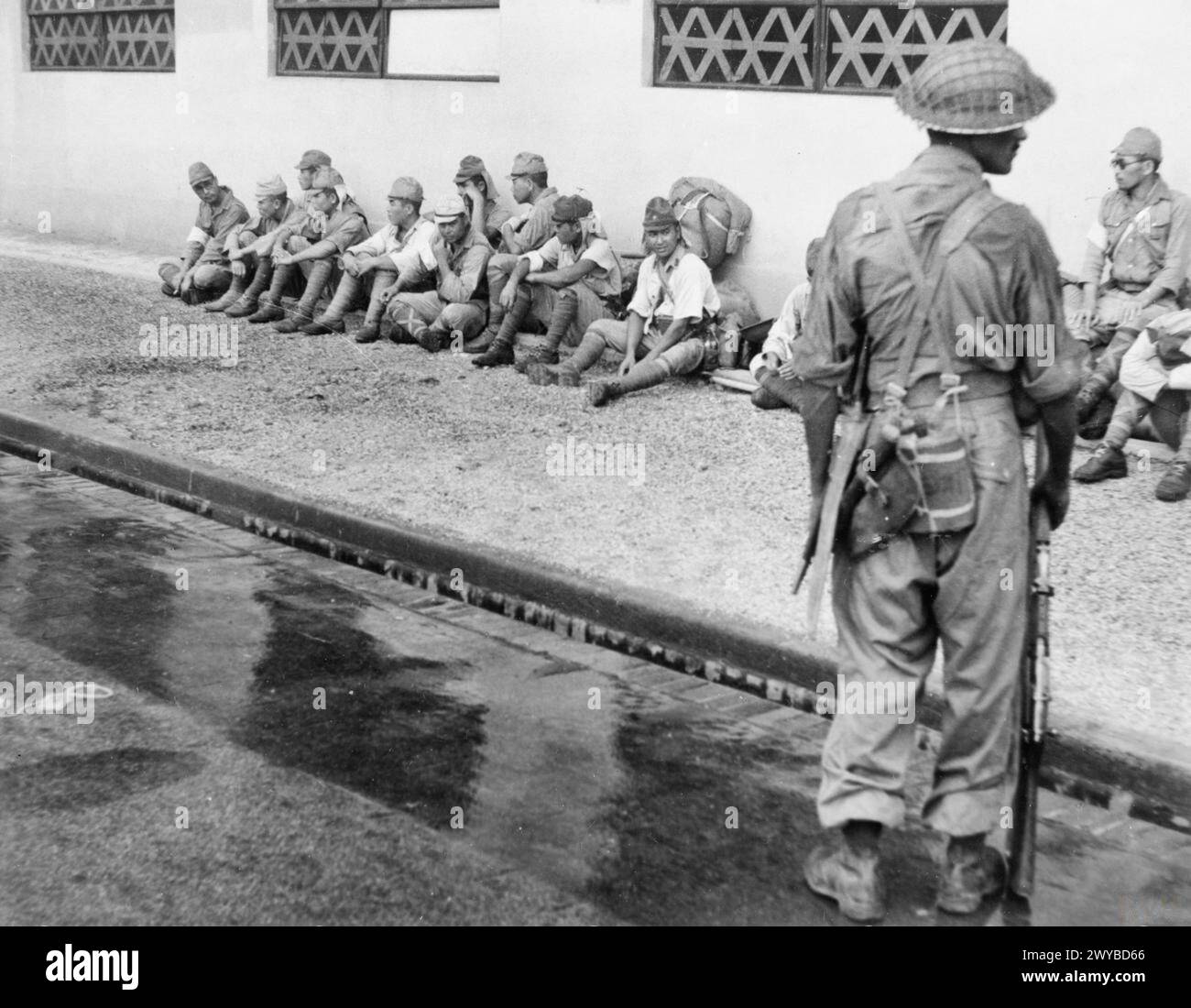 Nel 1945, un soldato della 5th Indian Division sorvegliò i prigionieri giapponesi fuori dal loro ex quartier generale durante la rioccupazione britannica di Singapore. Foto Stock