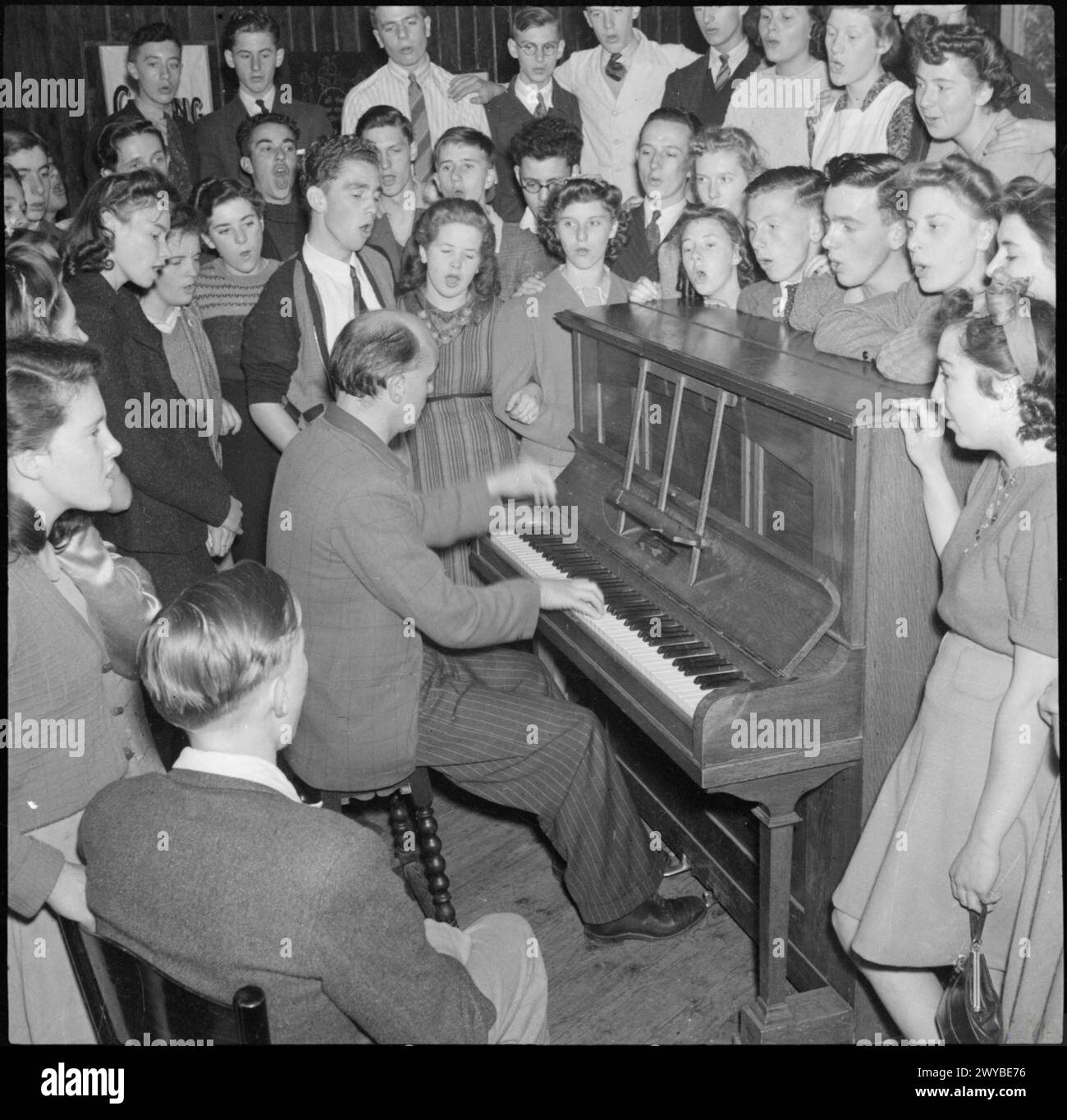 I giovani frequentano la Co-operative Union Summer School presso la Craig School, Windermere, Inghilterra, nel 1943, partecipando a sessioni musicali tra cui canto del coro e esibizioni di pianoforte guidate da un insegnante. Foto Stock