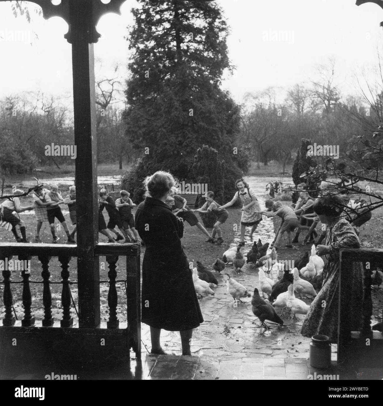 La signora R, agente del Welfare per il distretto rurale di High Wycombe, visita un ostello locale evacuato nel Buckinghamshire, Inghilterra, 1944 anni, osservando i bambini giocare e polli che forniscono uova. Foto Stock