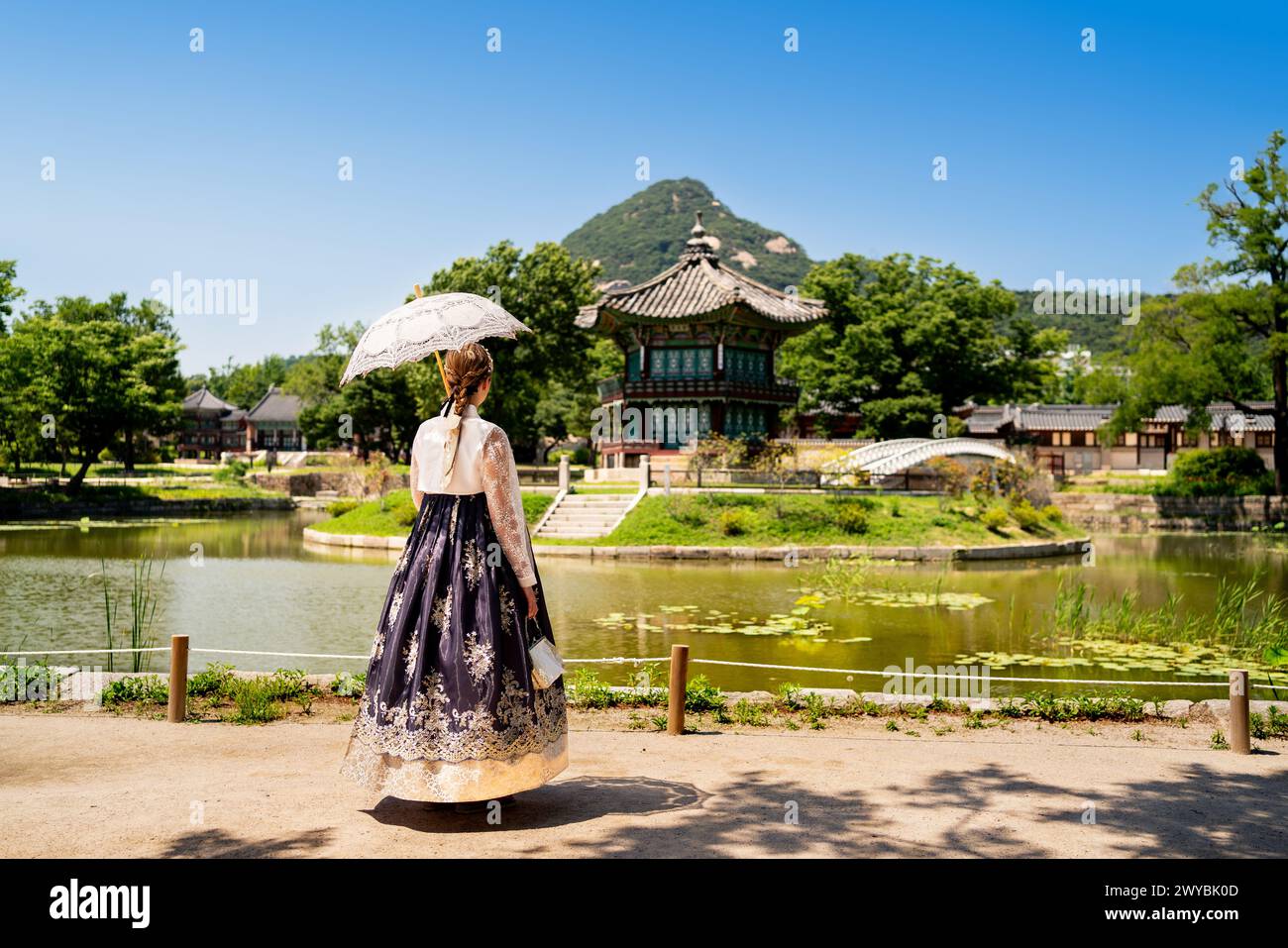 Seoul, Corea del Sud. Hanbok che indossa una donna. Giardino del parco del palazzo Gyeongbokgung. Tradizione coreana dell'abbigliamento. Padiglione Hyangwonjeong sullo sfondo. Foto Stock