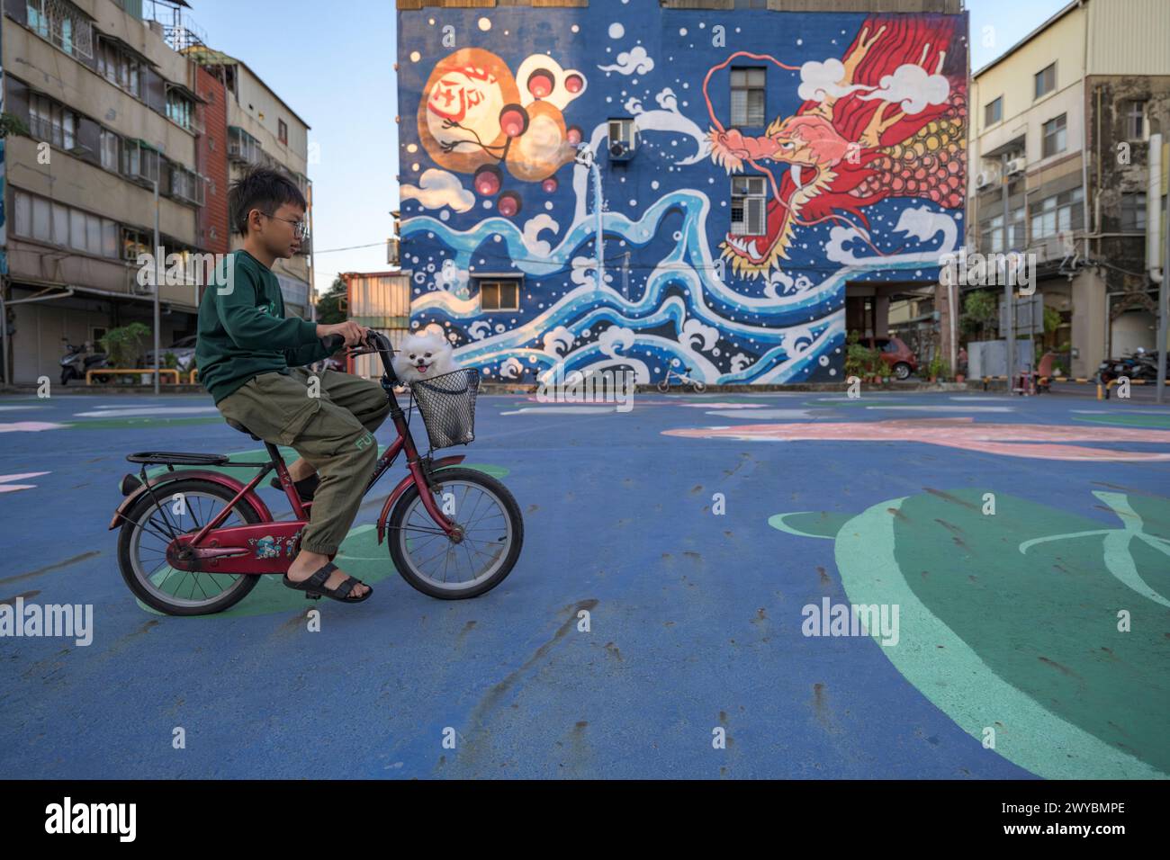 Un ragazzo passa in bicicletta con il suo cane davanti a un grande murale colorato di drago in un parco giochi della città di Tainan Foto Stock
