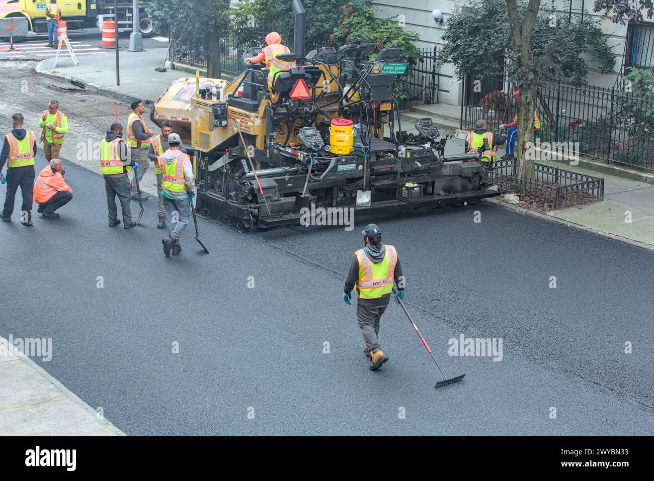 il lavoratore cittadino pavimenta la strada con un veicolo per pavimentazione (nuova installazione di asfalto su strade urbane) rullo vibrante tandem Foto Stock