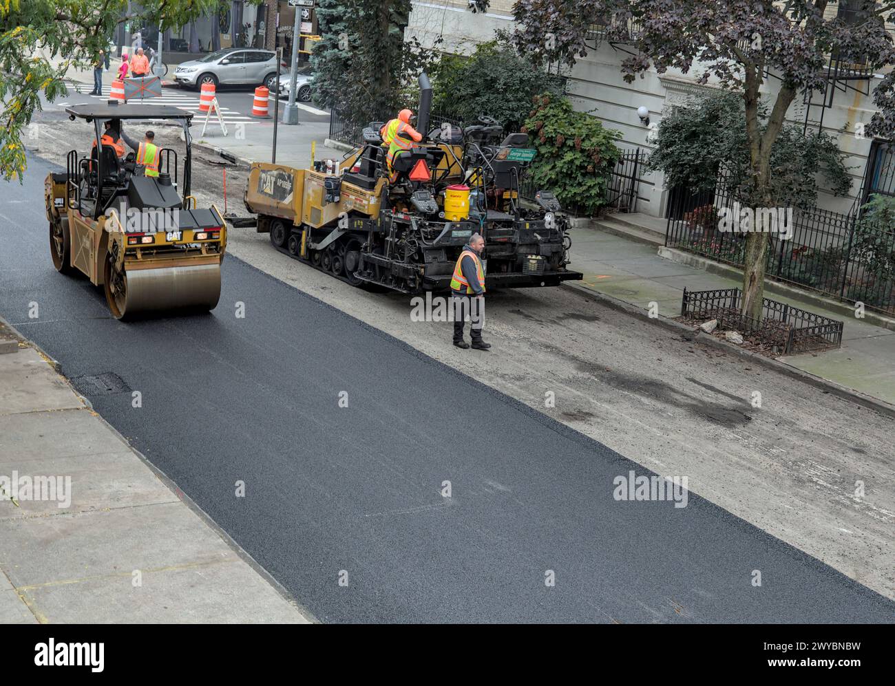 il lavoratore cittadino pavimenta la strada con un veicolo per pavimentazione (nuova installazione di asfalto su strade urbane) rullo vibrante tandem Foto Stock