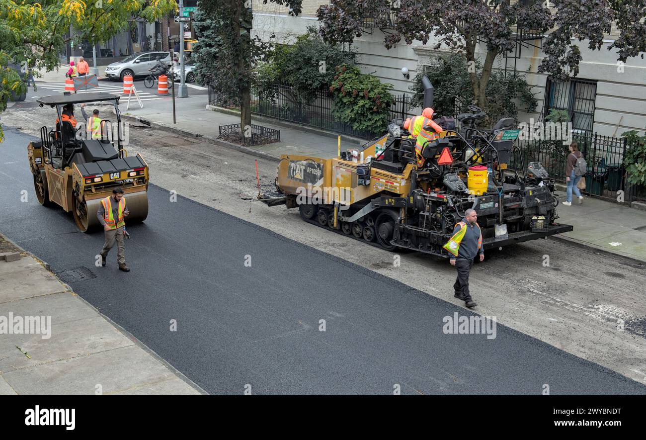 il lavoratore cittadino pavimenta la strada con un veicolo per pavimentazione (nuova installazione di asfalto su strade urbane) rullo vibrante tandem Foto Stock