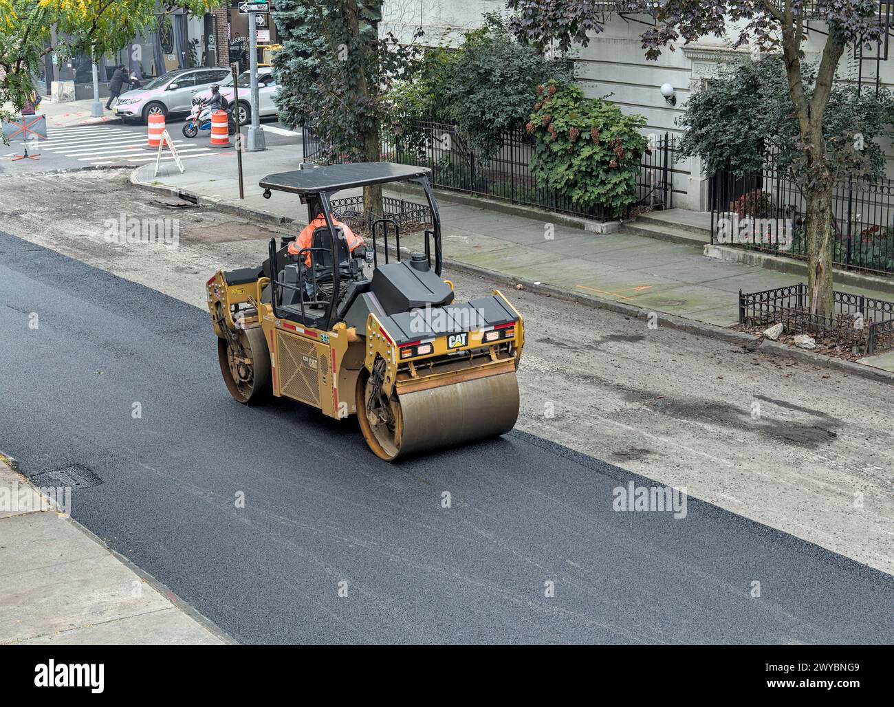 il lavoratore cittadino pavimenta la strada con un veicolo per pavimentazione (nuova installazione di asfalto su strade urbane) rullo vibrante tandem Foto Stock