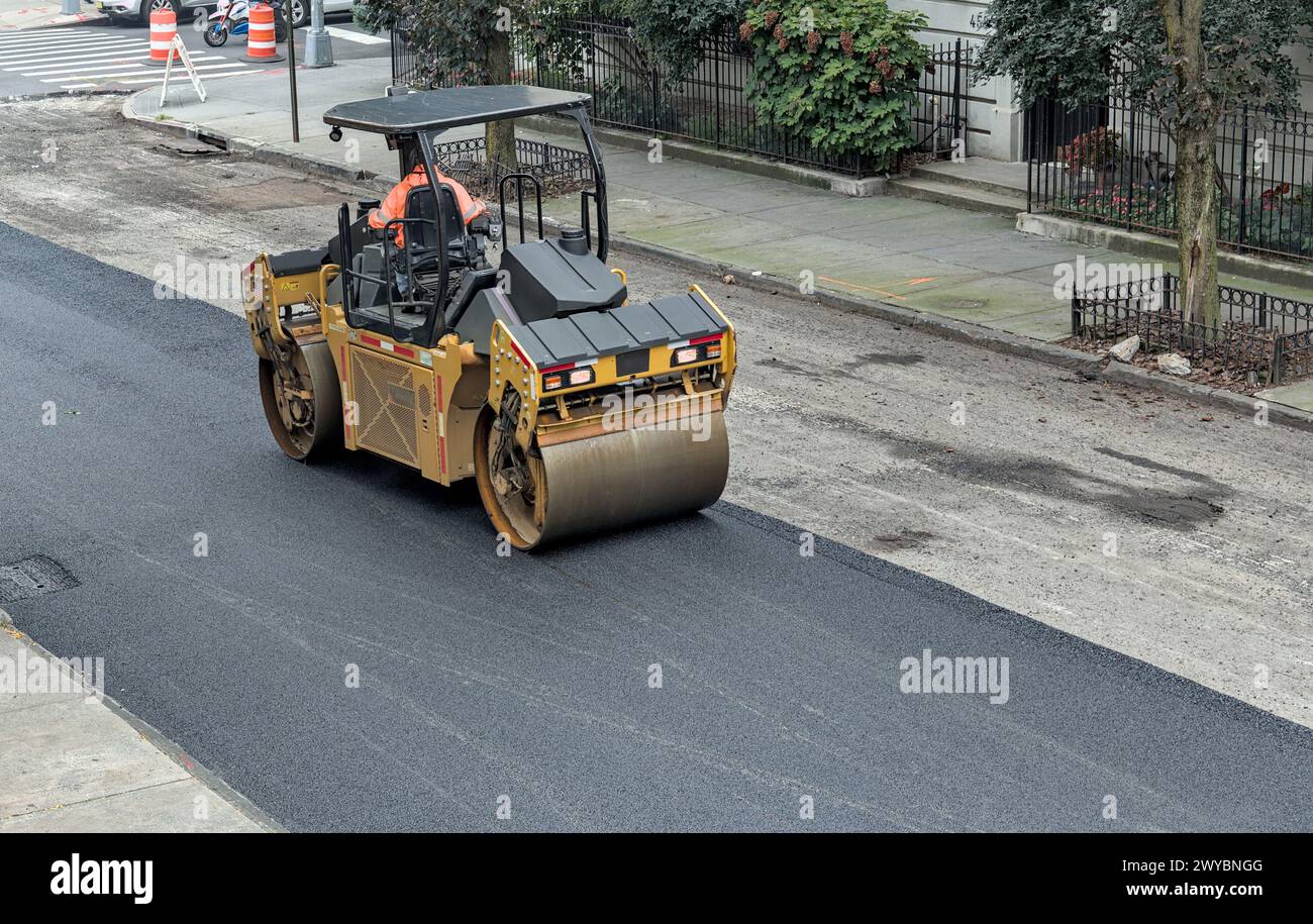 il lavoratore cittadino pavimenta la strada con un veicolo per pavimentazione (nuova installazione di asfalto su strade urbane) rullo vibrante tandem Foto Stock